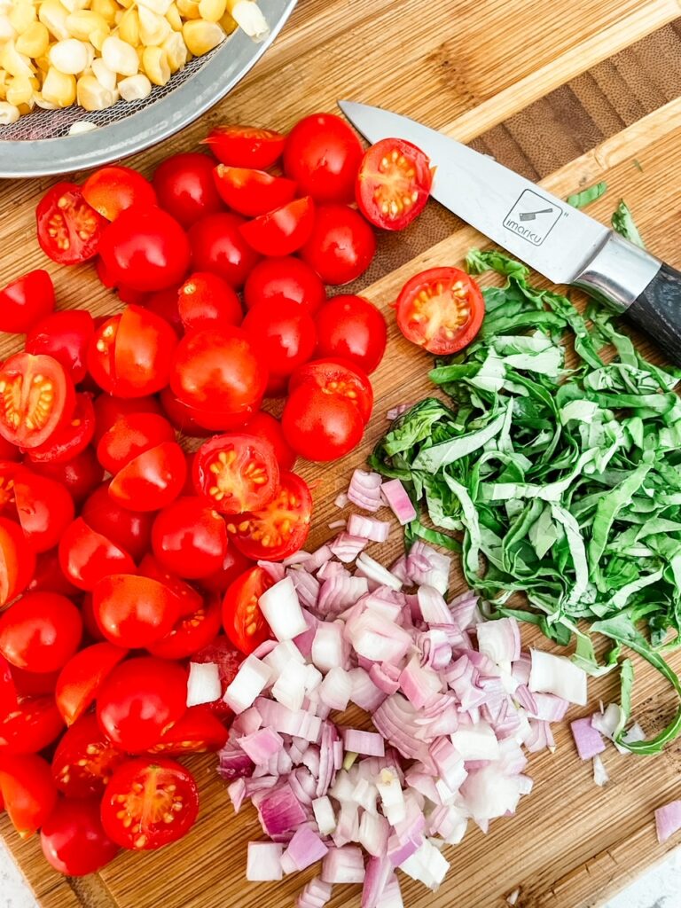 Chopped cherry tomatoes, basil, and shallots on a cutting board