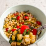 A bowl of the Fresh Corn and Cherry Tomato Salad, with a spoon holding up a portion of it