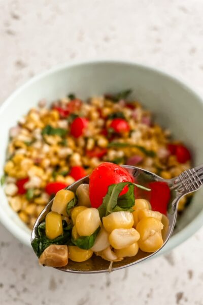 A bowl of the Fresh Corn and Cherry Tomato Salad, with a spoon holding up a portion of it