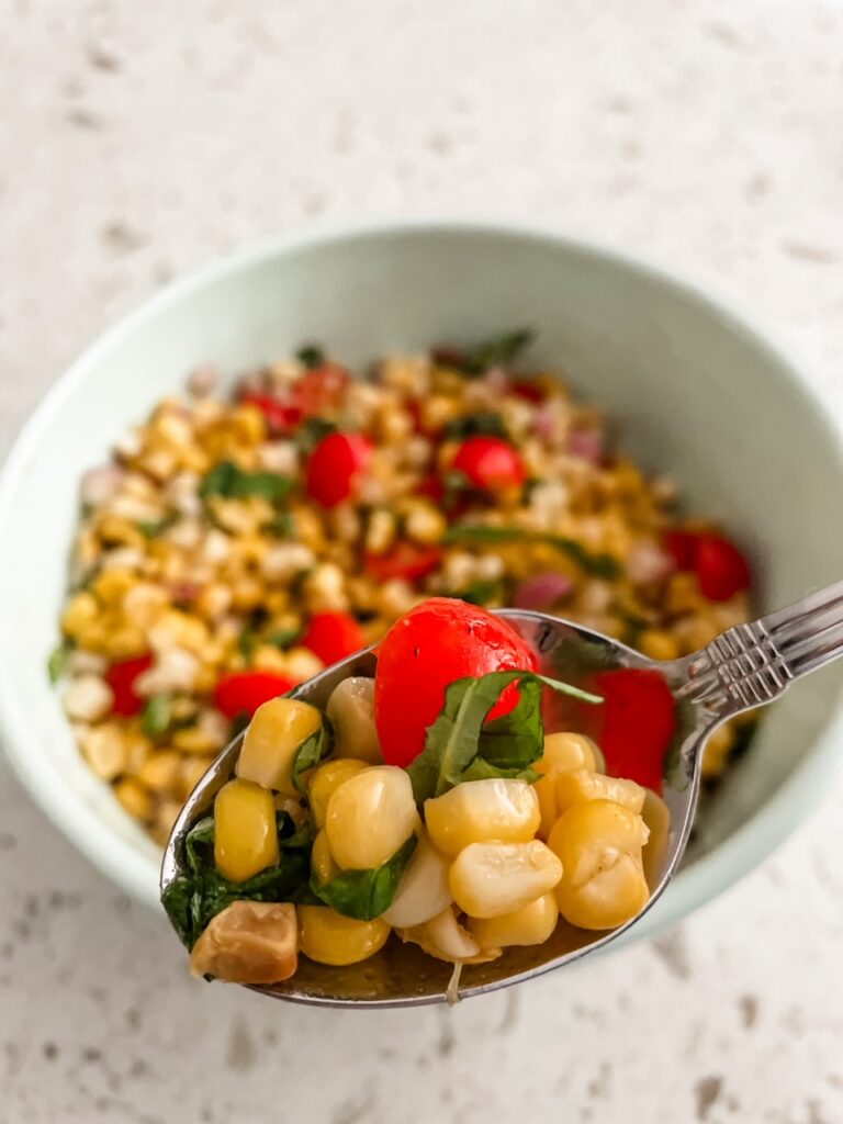 A bowl of the Fresh Corn and Cherry Tomato Salad, with a spoon holding up a portion of it