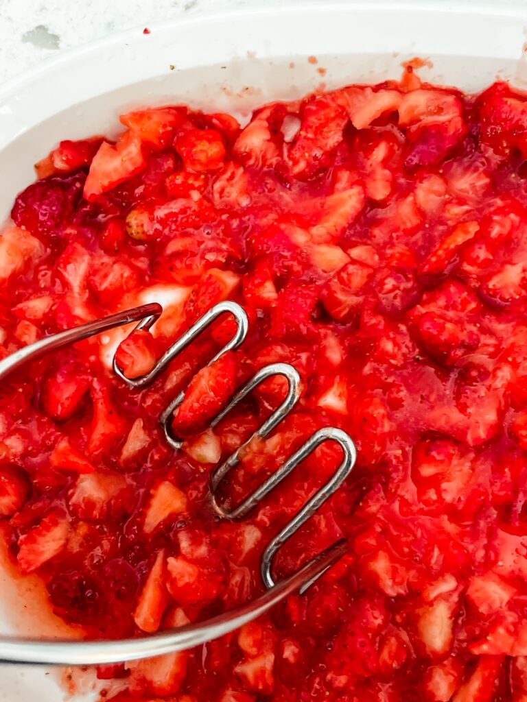 The sliced strawberries being smashed with the sugar