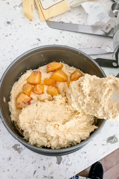 The peaches being mixed in between layers of batter in a pan