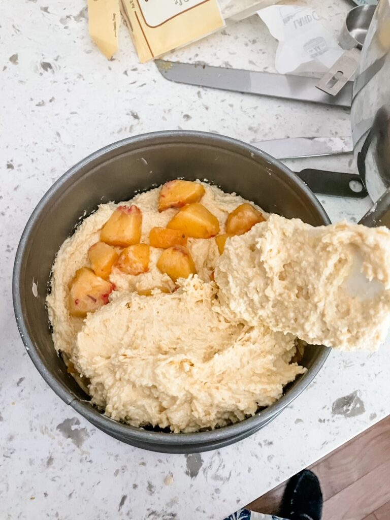 The peaches being mixed in between layers of batter in a pan