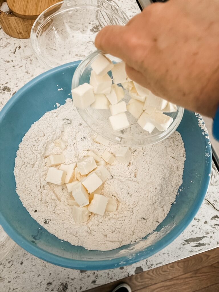 The cold chopped butter being placed in the bowl of dry ingredients