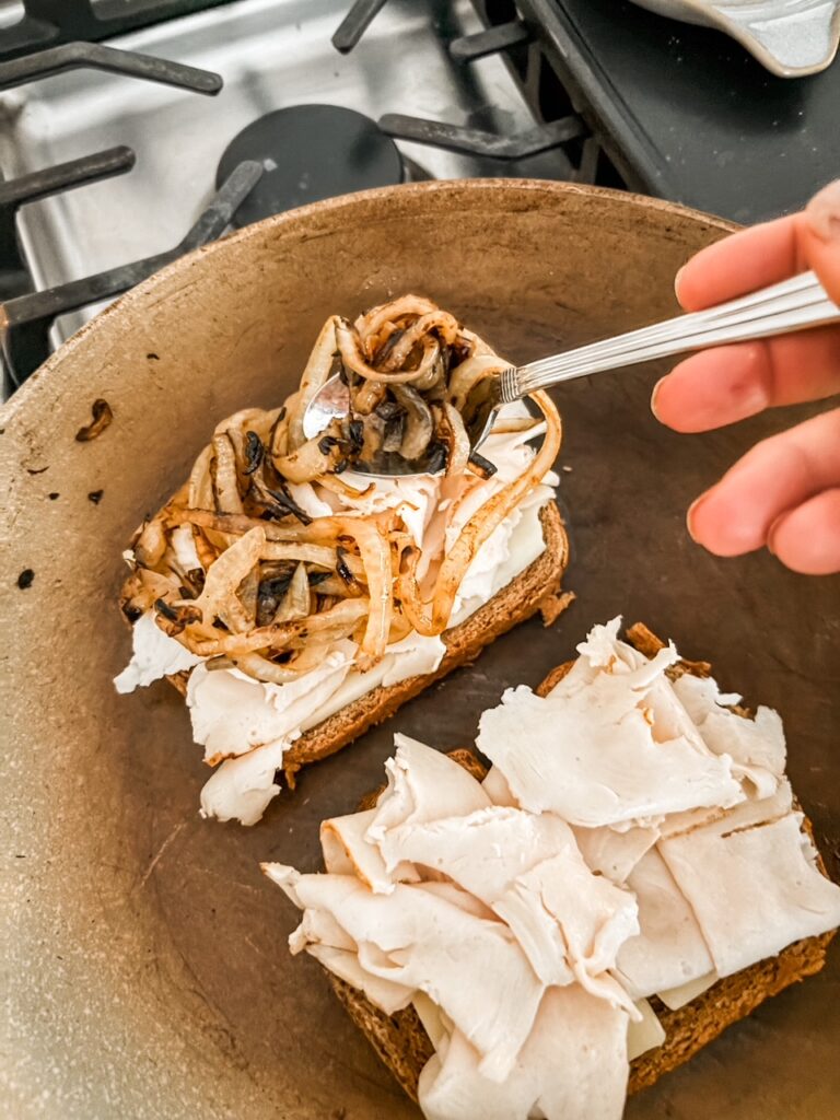 The sandwich being assembled with chicken, cheese, and onion