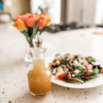 The Maple Vinaigrette Dressing in a bottle next to a plate of salad
