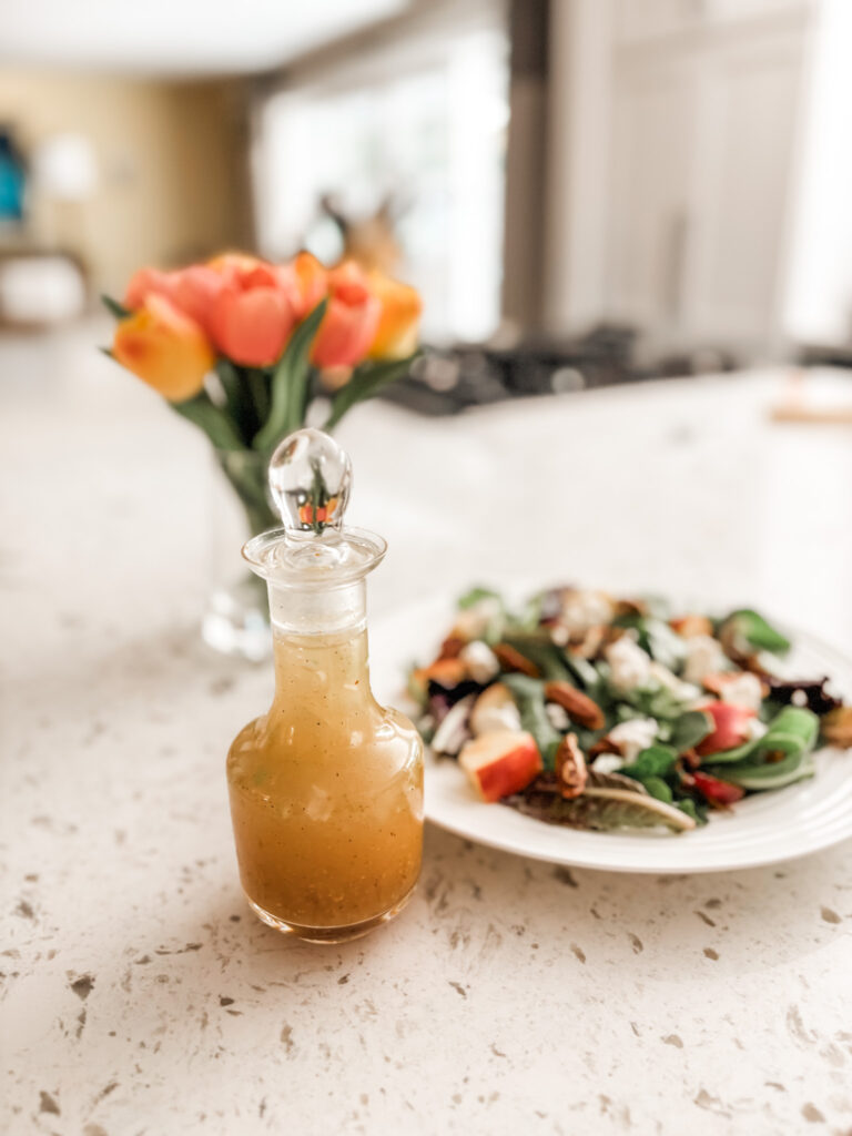 The Maple Vinaigrette Dressing in a bottle next to a plate of salad