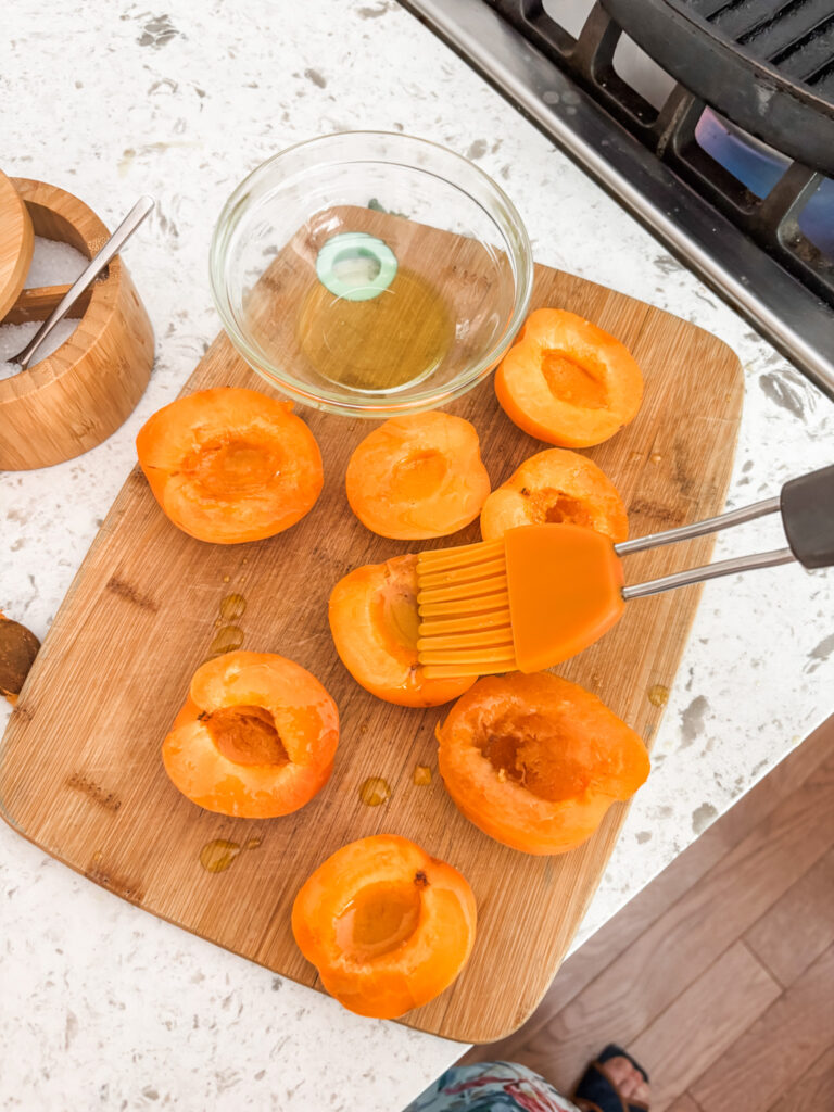 The apricots, sliced in half and being brushed with olive oil