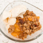 The finished Gluten-Free Peach Crumble Dessert in a serving bowl with ice cream
