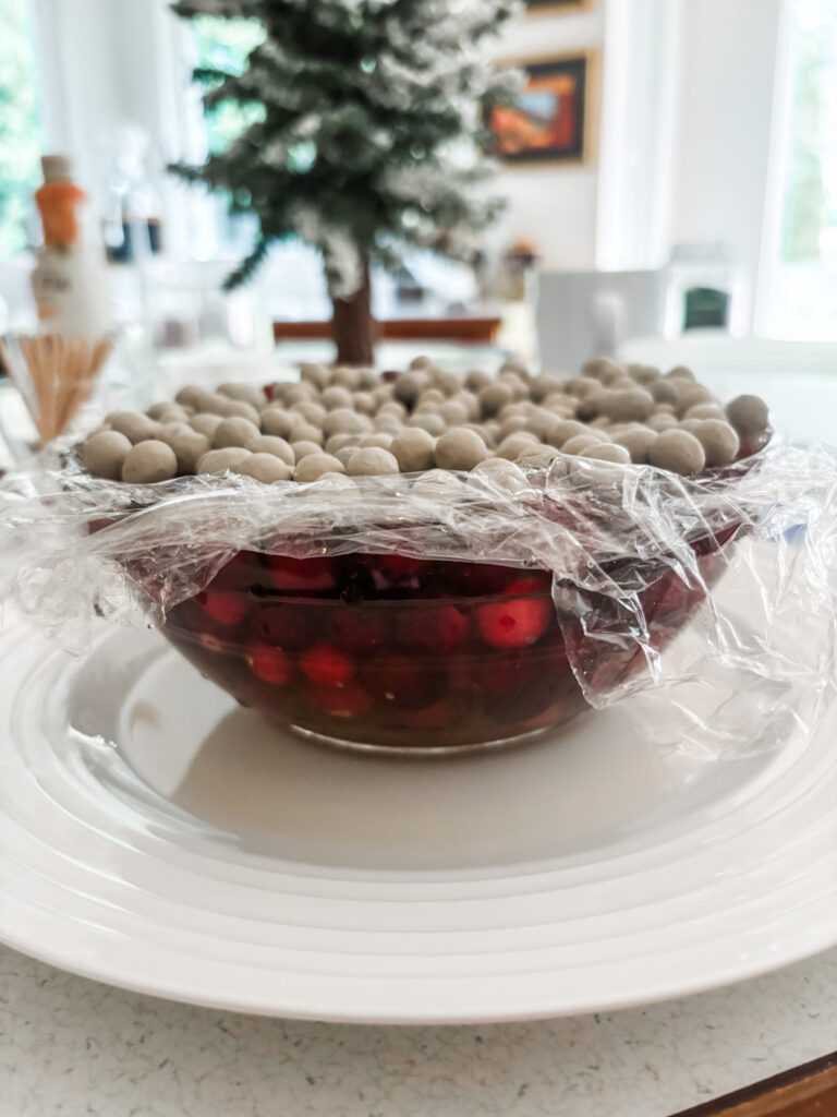 The cranberries being forced into the soaking mixture with a layer of saran wrap and dried beans