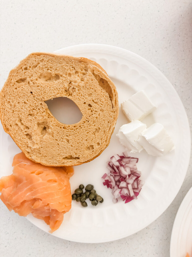 A bagel on a plate with lox, onion, and capers