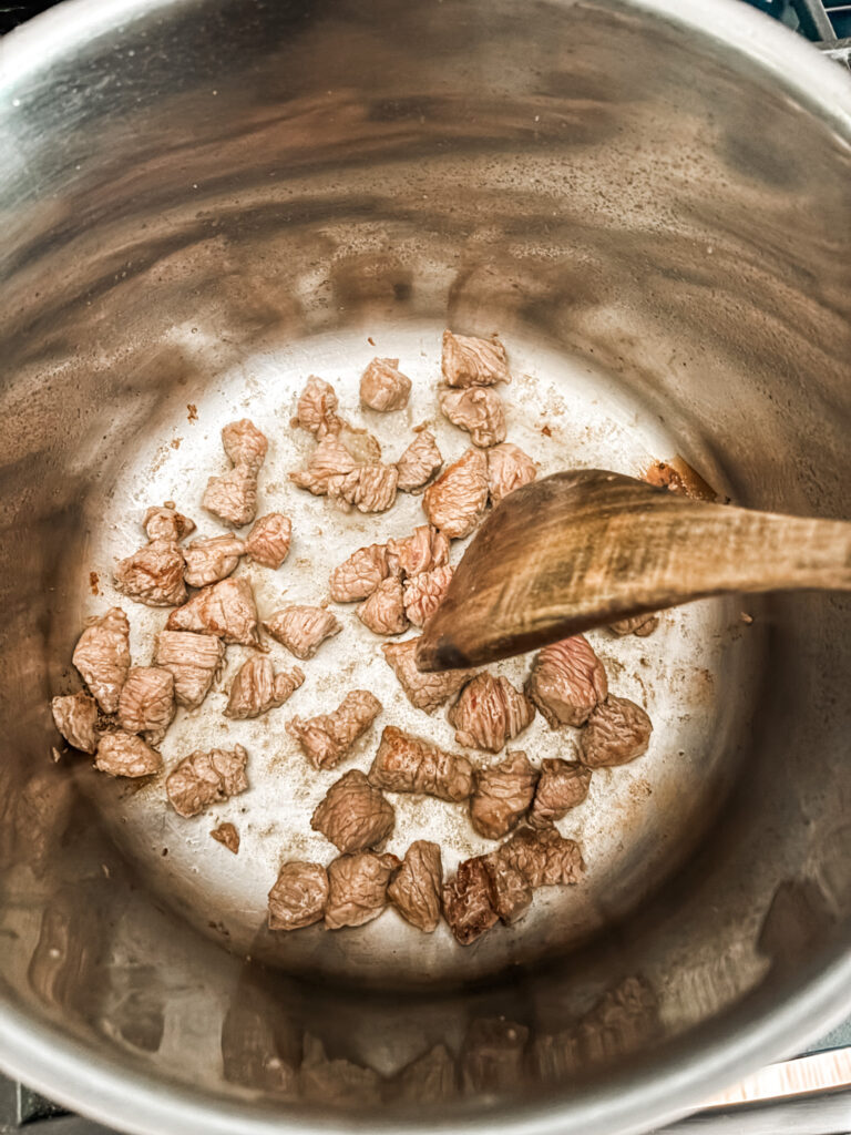 The beef pieces browning in a pan