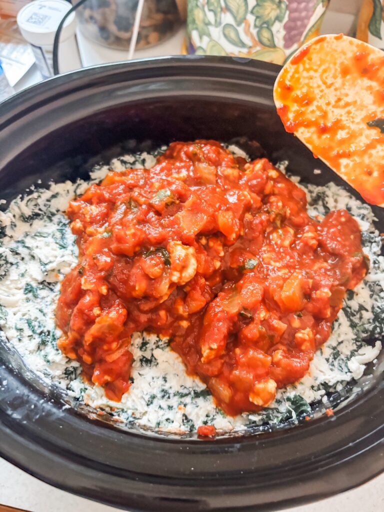 The sauce and cheese mixture being layered into the slow cooker