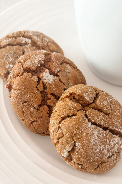 Three chewy triple ginger molasses cookies stacked on a white plate next to a white mug, dusted with sparkling sugar