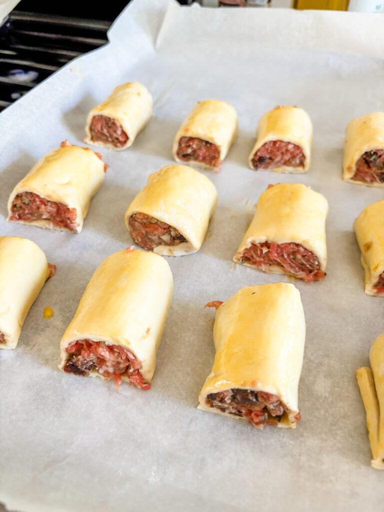 The prepared sausage rolls, ready for baking on a parchment lined baking sheet
