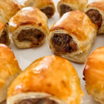 Sliced sausage roll showing savory sausage filling with visible pieces of Medjool dates and rosemary inside flaky pastry