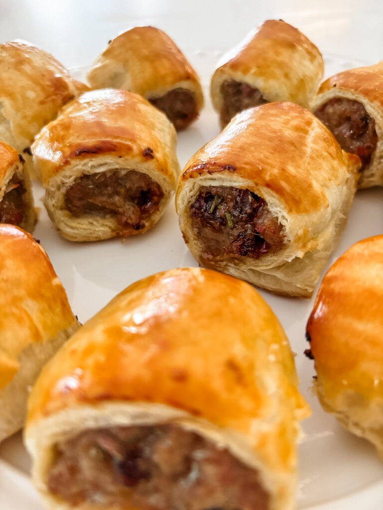 Sliced sausage roll showing savory sausage filling with visible pieces of Medjool dates and rosemary inside flaky pastry