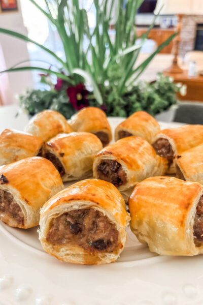 Golden baked sausage rolls with date and rosemary arranged on a white serving platter