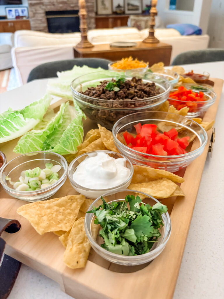 Low-carb taco board with romaine lettuce cups, seasoned beef, and colorful toppings arranged on a large wooden serving board