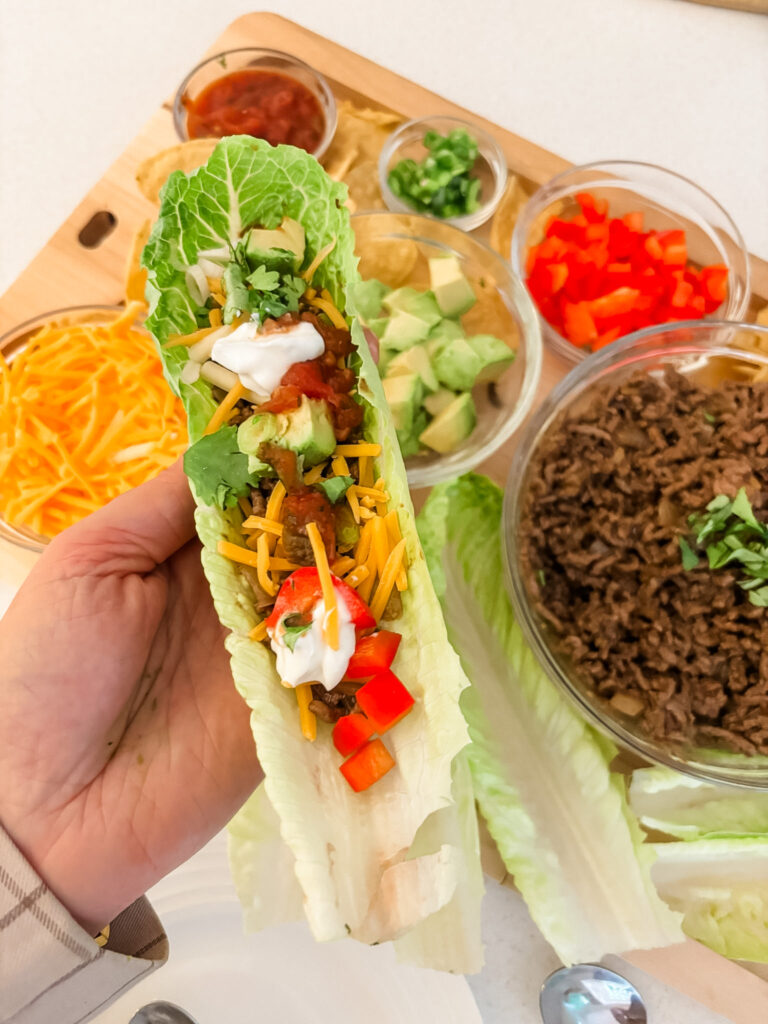 Hand holding a low-carb romaine lettuce taco cup loaded with seasoned beef and toppings