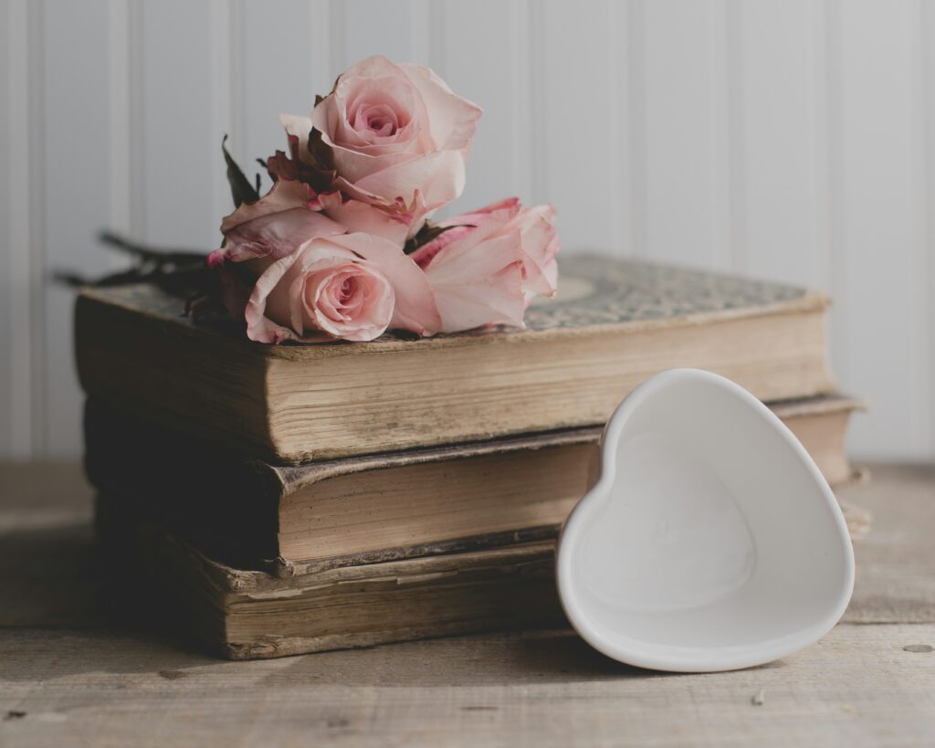 A stack of old books with roses on top and a heart dish leaning against them