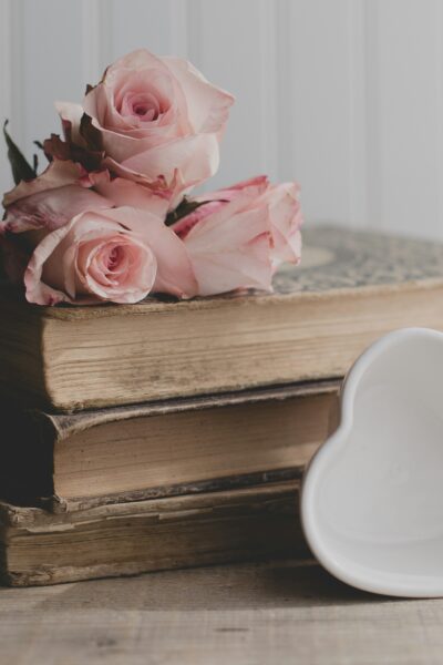 A stack of old books with roses on top and a heart dish leaning against them