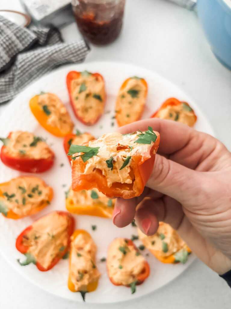 Colorful stuffed mini bell peppers filled with cream cheese and hot pepper jelly arranged on a white serving platter with one being held up
