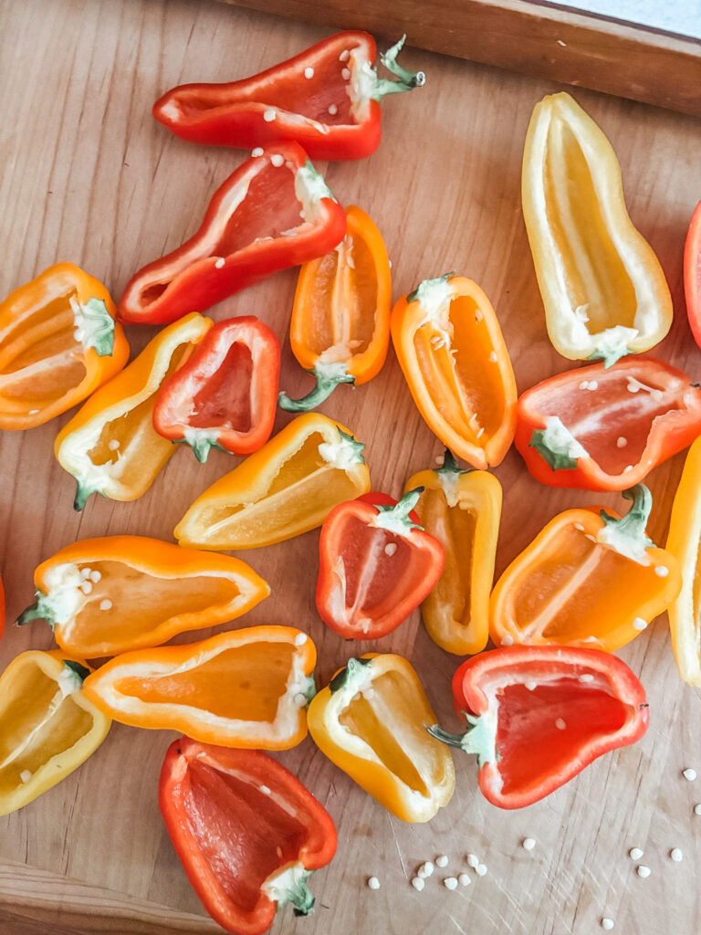 Halved and seeded red, yellow, and orange mini bell peppers laid out on a cutting board ready to be filled