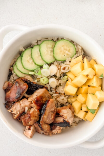 Mango chicken coconut rice bowl topped with fresh mango, sliced cucumber, scallions, and cilantro over coconut lime jasmine rice