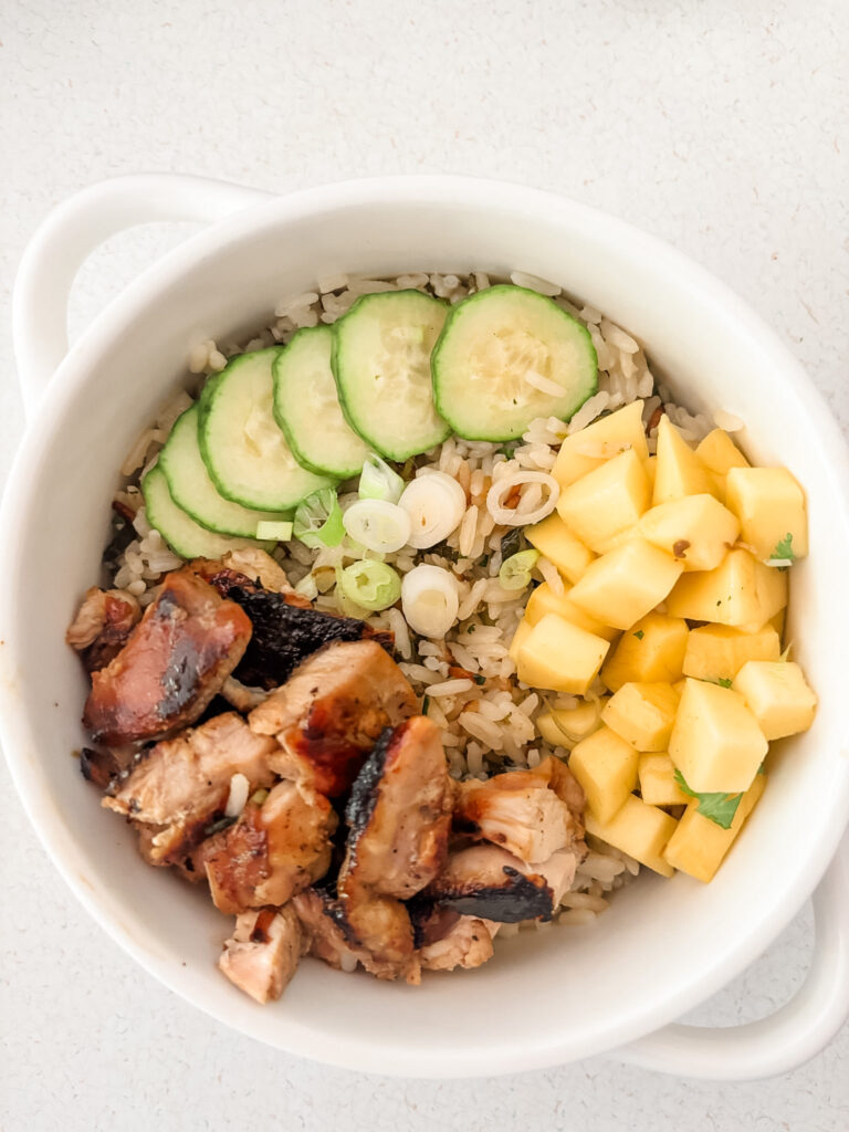 Mango chicken coconut rice bowl topped with fresh mango, sliced cucumber, scallions, and cilantro over coconut lime jasmine rice