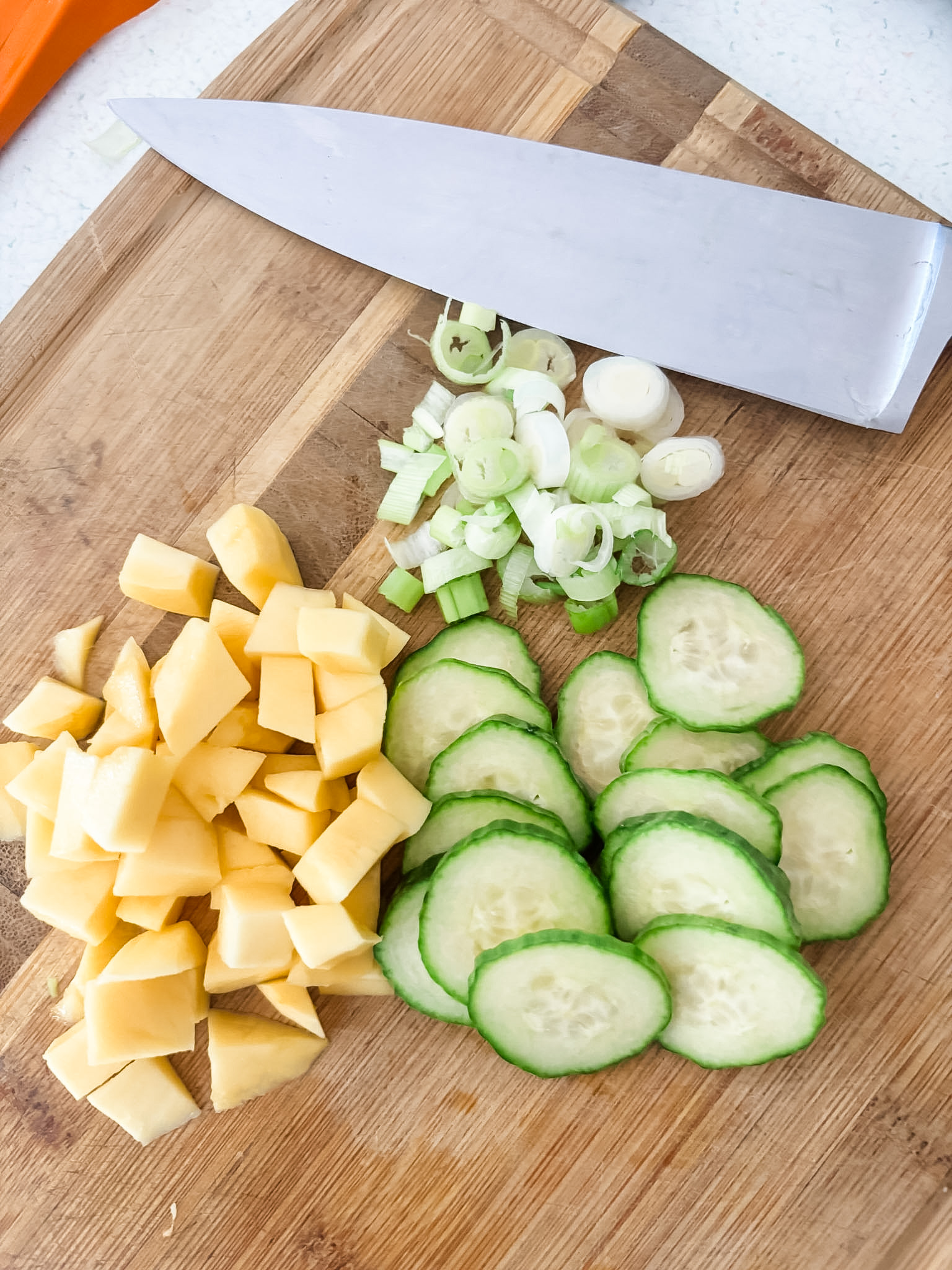 The chopped and sliced mango, cucumber, and green onion on a wooden cutting board