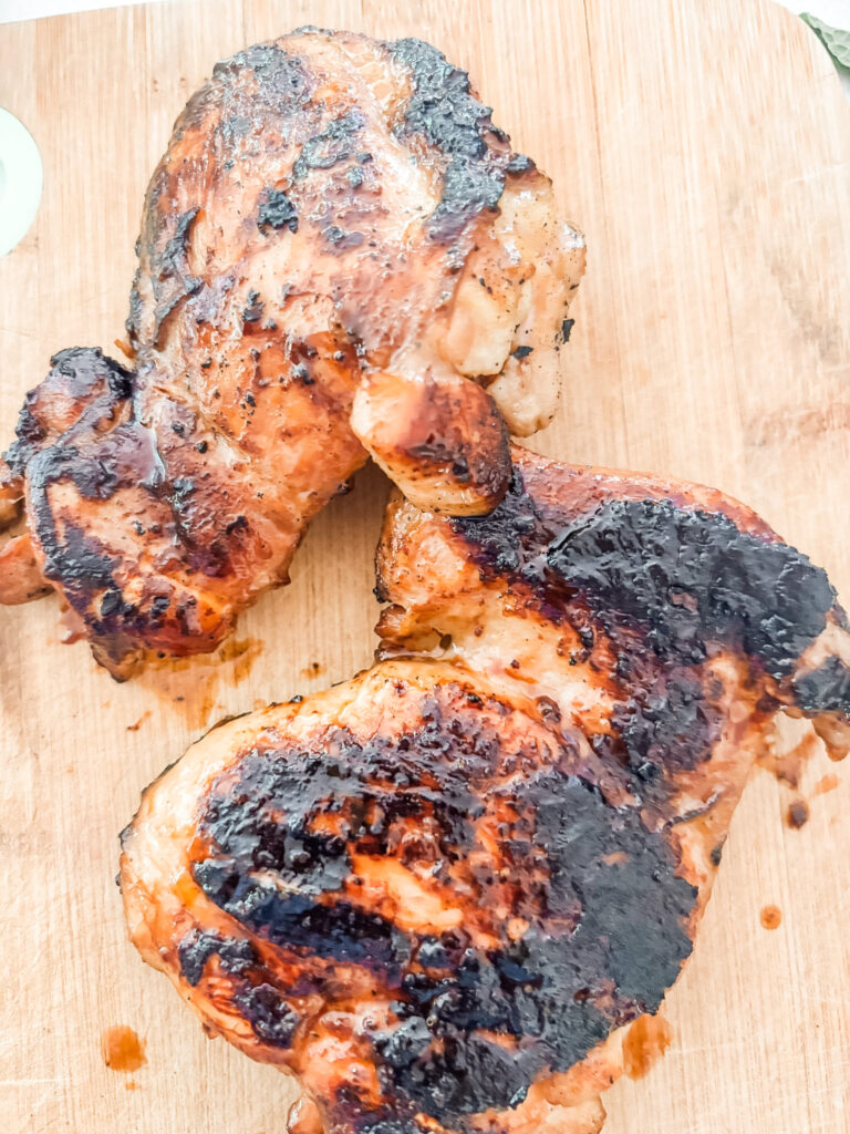 The marinated and broiled chicken thighs on a wooden cutting board