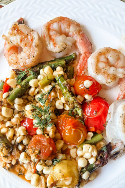 Springtime succotash with lemon and dill served alongside grilled shrimp on a white dinner plate