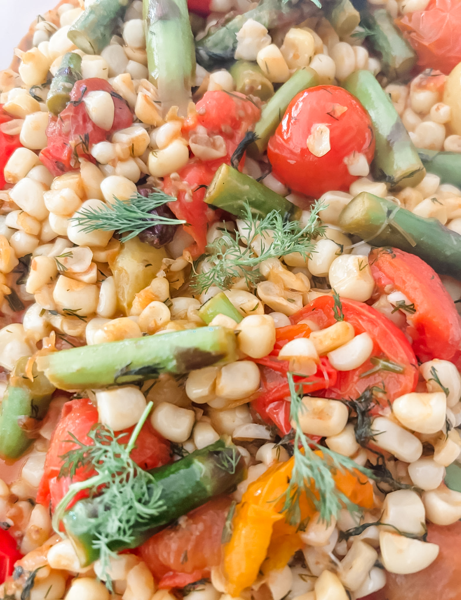 Close-up of springtime succotash with bright green asparagus, golden corn kernels, and burst cherry tomatoes garnished with fresh dill