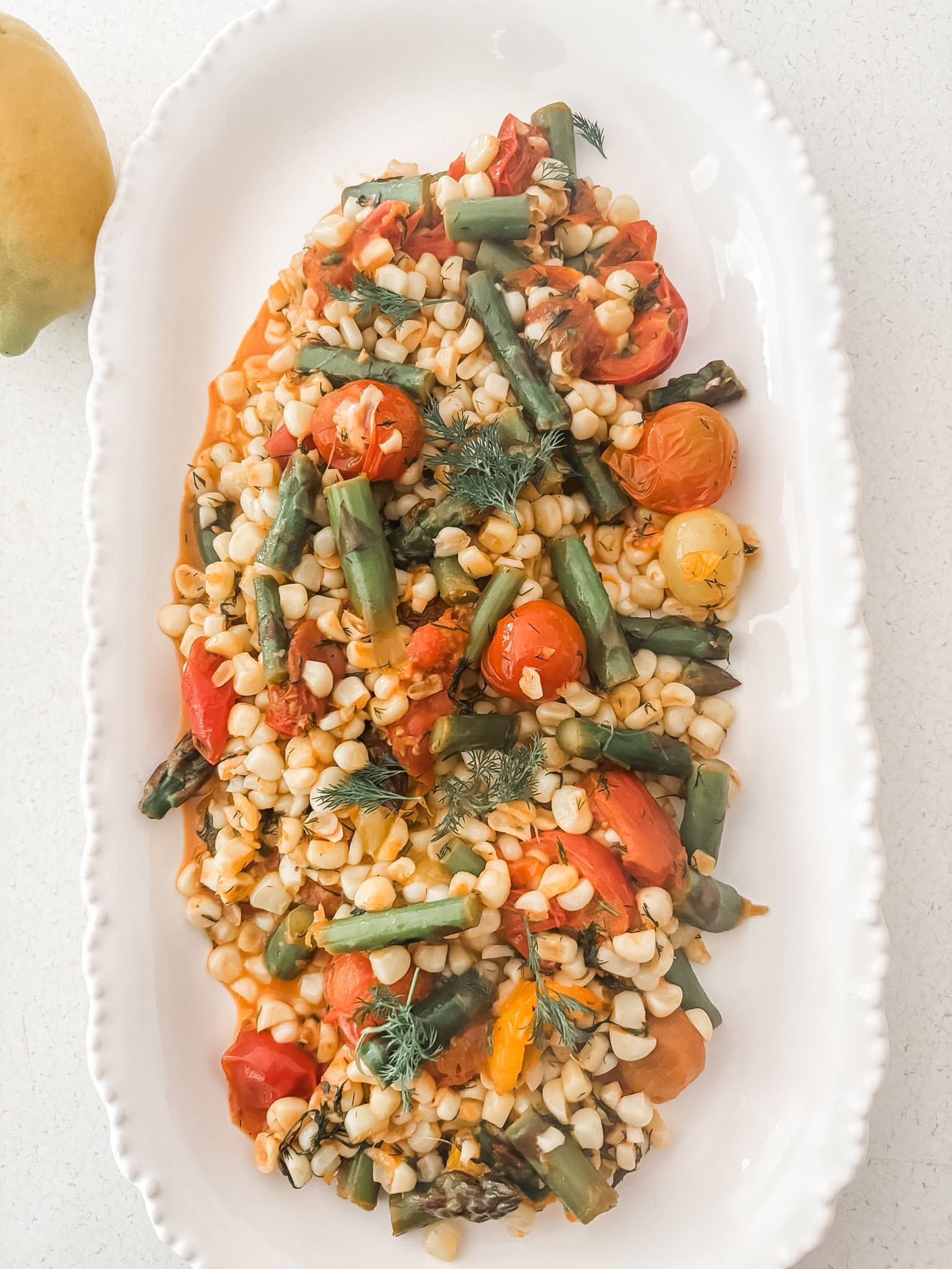 Springtime succotash with corn, asparagus, and cherry tomatoes in a lemon dill butter sauce served in a white bowl