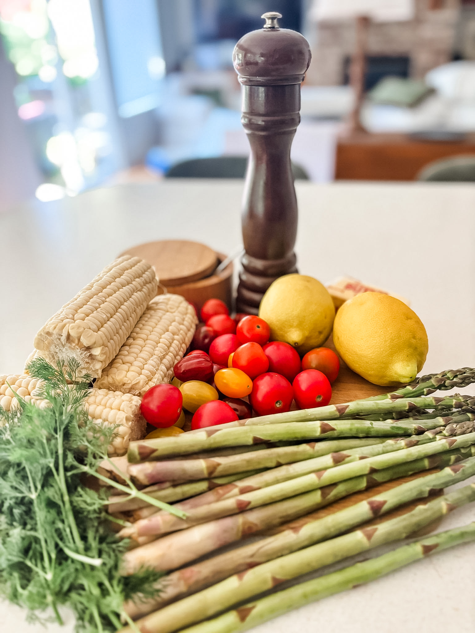 Fresh ingredients for springtime succotash including corn on the cob, asparagus stalks, cherry tomatoes, fresh dill, lemon, and butter