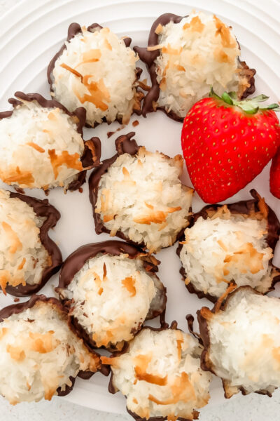 Close-up of a chocolate-dipped coconut macaroon showing its golden toasted exterior and dark chocolate base with strawberries