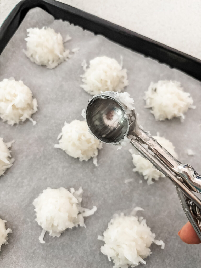Using a melon baller to shape coconut macaroon mixture into uniform balls on a parchment-lined baking sheet