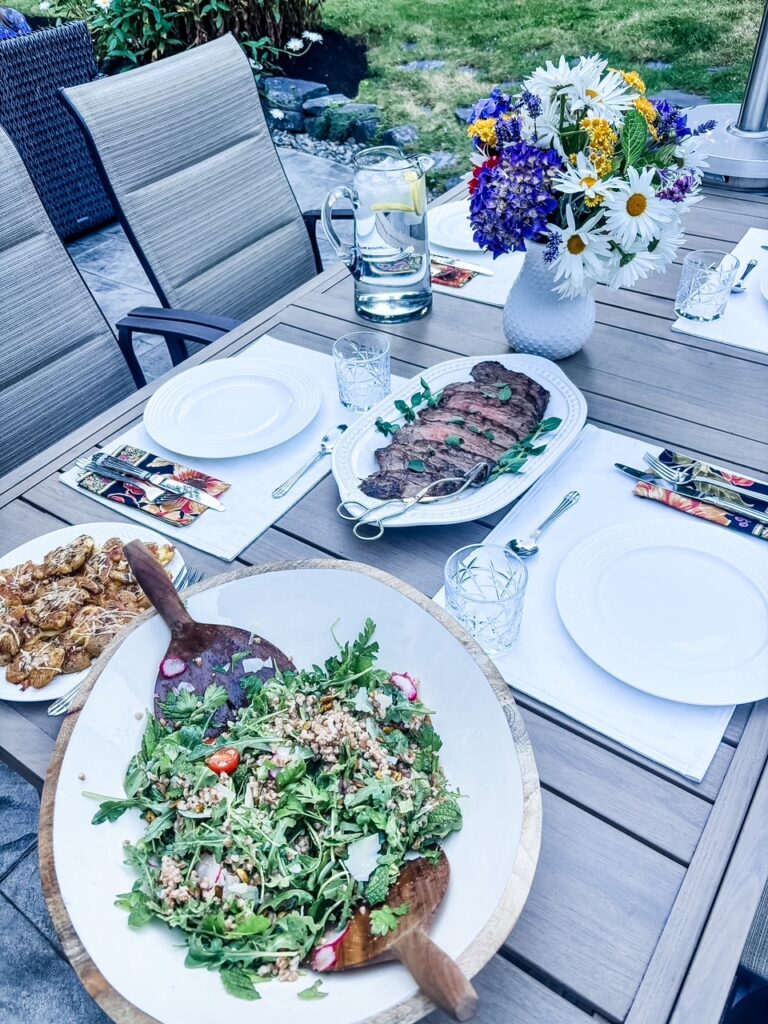 The salad served at a summer al fresco table set with plates and servings of steak