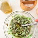 A glass jar of fresh chimichurri sauce with chopped parsley, oregano, minced garlic, and red pepper flakes in olive oil