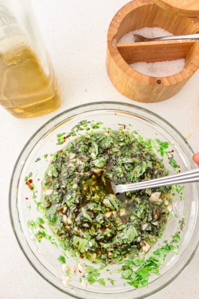 A glass jar of fresh chimichurri sauce with chopped parsley, oregano, minced garlic, and red pepper flakes in olive oil