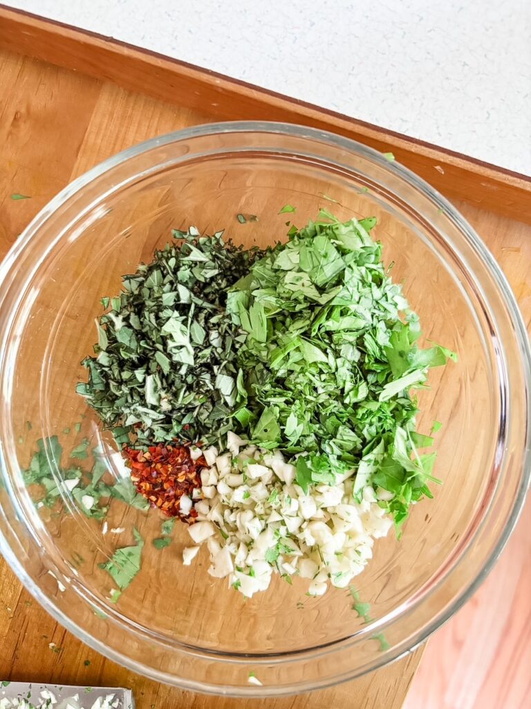 Freshly chopped parsley, garlic and oregano in a glass bowl on a wooden cutting board