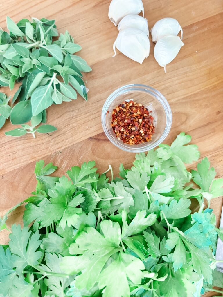 A glass jar of fresh chimichurri sauce with chopped parsley, oregano, minced garlic, and red pepper flakes in olive oil