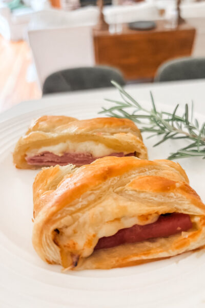 Sliced ham and cheese strudel on a white serving board showing flaky golden pastry and melted Swiss cheese filling