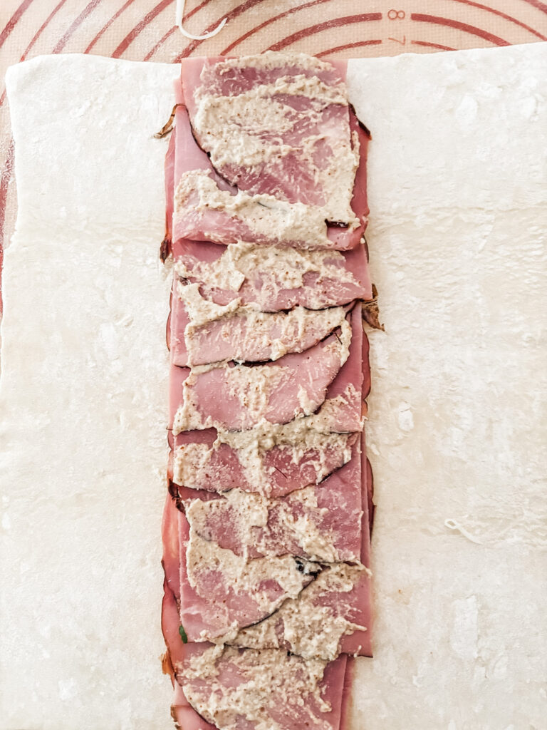 Thin-sliced deli ham layered down the center of a rolled puff pastry sheet with mustard and shredded Swiss cheese