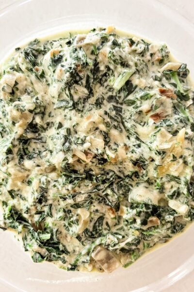Creamed kale and carrot tops in a rich parmesan cream sauce served in a white bowl