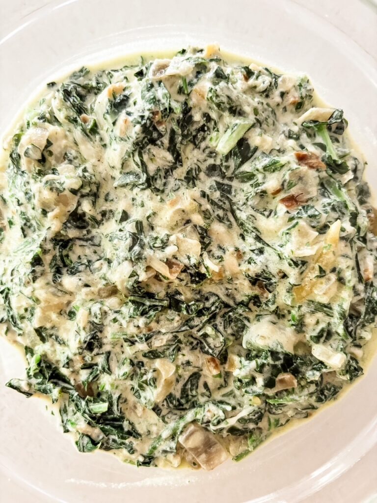 Creamed kale and carrot tops in a rich parmesan cream sauce served in a white bowl