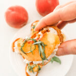 Close-up of a single peach crostini with chèvre, a peach slice, balsamic drizzle, and basil ribbons