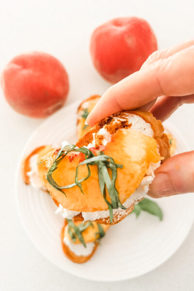 Close-up of a single peach crostini with chèvre, a peach slice, balsamic drizzle, and basil ribbons