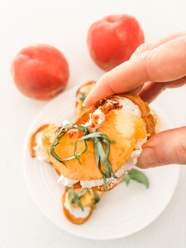 Close-up of a single peach crostini with chèvre, a peach slice, balsamic drizzle, and basil ribbons